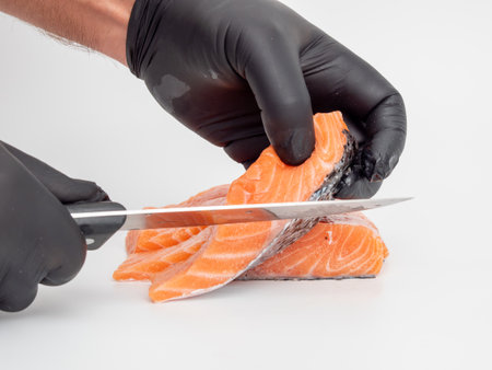 A chef in a black glove cuts salmon on a white background. Red fish fillet close-up. Selective focus.の写真素材