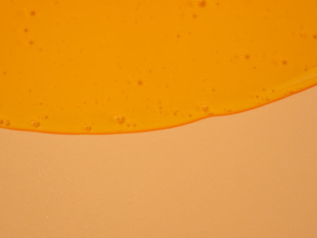 Liquid shower gel flows gracefully across a bright orange background. The translucent waves of the shower gel create a captivating visual symphony. Liquid shower gel flows over an orange background.の写真素材