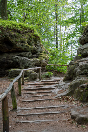 A wooden staircase leads up a rocky hillside. The path is surrounded by trees and the sky is cloudyの写真素材
