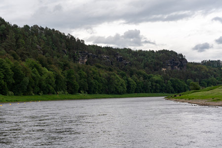 A river with a cloudy sky in the background. The water is calm and the trees are lushの写真素材