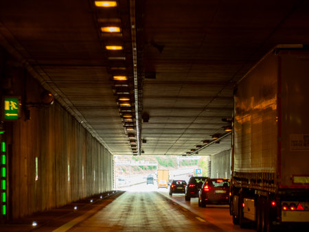 Germany May 17, 2024 Tunnel with green exit sign. The tunnel is dark and has several lights. Cars and a truck are driving through the tunnel.のeditorial素材