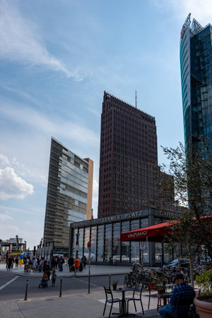 Germany Berlin June 07, 2024 Busy city street with a large building in the background. The street is filled with people walking and sitting at tables near the cafe.のeditorial素材