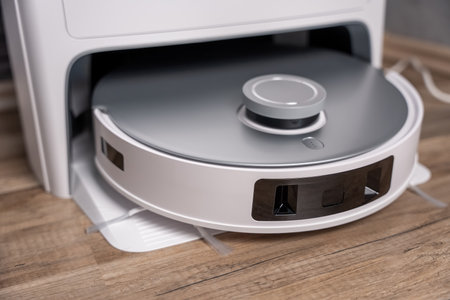 A white robot vacuum cleaner with a silver base. The robot is on a wooden floorの写真素材