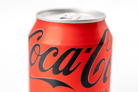 A can of Coca Cola is shown in a close up. The can is red and black with the Coca Cola logo on the...