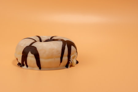 A chocolate covered doughnut sits on a table. The doughnut is placed on a table with a yellow backgroundの写真素材