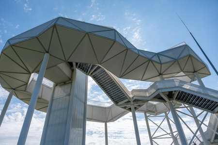 White observation tower with a spiral staircase. The structure is tall and has a lot of white. Blue...