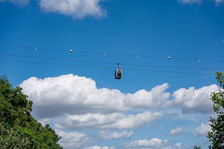 A cable car is flying through the sky above a forest. The sky is mostly clear, with a few clouds...