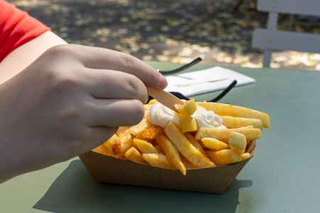 A person is eating french fries with a dipping sauce. The person is wearing a red shirt. The table is greenの写真素材