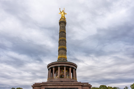 A tall, gold-covered tower with a statue of an eagle on top. The sky is cloudy and the sun is not visibleの写真素材