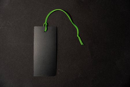 A black tag with a green rope hanging from it. The tag is empty and nothing is written on it. The label lies on a black background.の写真素材