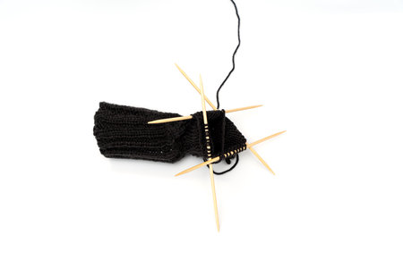 A black sock is made using a needle and a skein of yarn. Yarn on a white background.の写真素材