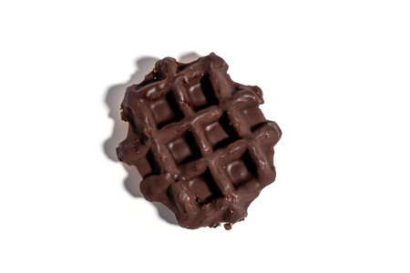 A chocolate waffle sits on a white background. The waffle is covered in chocolate and has a square shape Sweet pastries isolated on white background.の写真素材