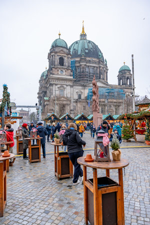 Germany Berlin December 26, 2024. A group of people are standing near a large building with a blue dome. People gather at tables, and there are potted plants and lanterns around. The scene is festive and lively.のeditorial素材