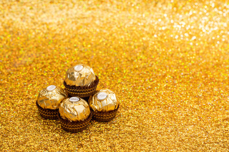 Ferrero Rocher chocolates in gold color sit on a gold background. The candies are arranged in a pyramid shape. The image has a warm toneのeditorial素材