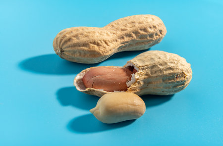 Peanuts are cut in half. Peanut halves are on a blue surface