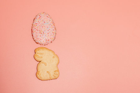 A cookie shaped like an Easter egg is on a pink background. There is another cookie shaped like a...