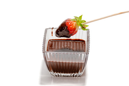 A bowl of chocolate sauce with a strawberry on a stick. The bowl is in front of a white backgroundの写真素材