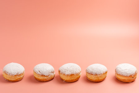 A row of donuts with powdered sugar on top. There are five donuts in total. The donuts are arranged in a line, with the first donut on the left and the last one on the rightの写真素材