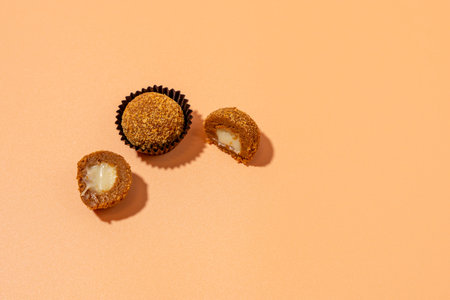 Honey ball in brown wrapper and next to it cut in half with milk filling on orange background. Candies on orange background.の写真素材