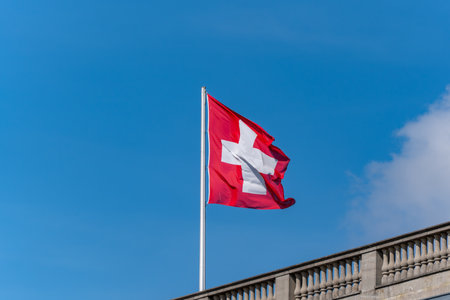 A red and white flag with a cross on it is flying in the sky. The flag is on a pole and is visible from a distanceの写真素材