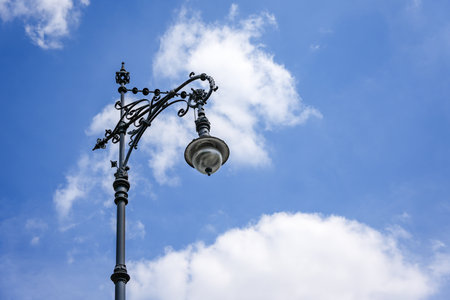 Decorative, artistically curved historic street lamp against a blue sky with light clouds. A typical detail of Berlin's urban architecture.の写真素材