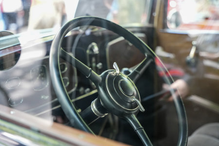 A close-up of a classic steering wheel inside a vintage car, viewed through the window. The interior shows wooden paneling and traditional controls, evoking a sense of historical craftsmanship.の写真素材