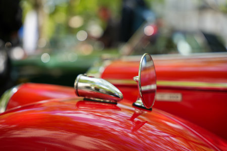 A polished red vintage car fender with a chrome bullet-shaped mirror. With a reflective green surround and capturing the smooth lines.の写真素材