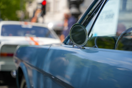 Side view of a classic blue car with the round chrome side mirror in focus. Blurred street in the background.の写真素材