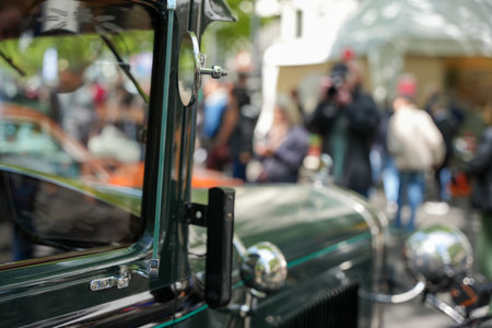 Green vintage car and crowd at a car show. Old green car with round headlight and chrome elements in the foreground, blurred crowd of people and photographers in the background.の写真素材