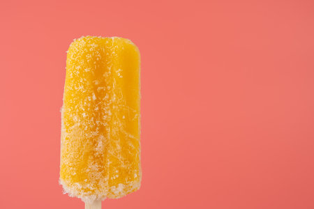 A single frozen mango popsicle with ice crystals against a bright pink background. The contrasting...