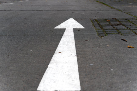 Straight-ahead arrow on asphalt. A white directional arrow is clearly visible on the asphalt of a road, pointing straight ahead. The image conveys movement and orientation in an urban space.の写真素材