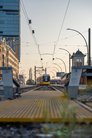 A yellow Berlin tram approaches on straight tracks in the soft evening light. Buildings and power lines frame the scene symmetrically.の写真素材