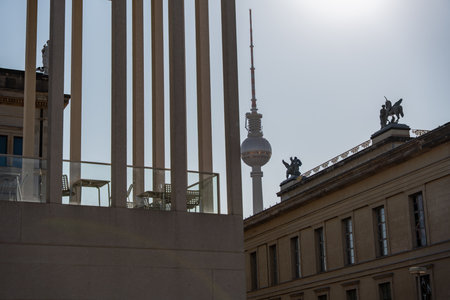 The Berlin TV tower is visible through modern columns, next to it are historic museum buildings with roof sculptures. The perspective emphasizes the contrast between old and new.の写真素材