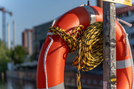 An orange lifebuoy with a yellow rope is attached to a post. The scene depicts safety precautions on the water.の写真素材