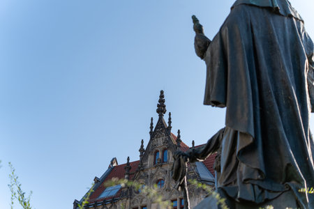 A statue in front of a historic building with ornate gables and a red roof. The angle emphasizes the height and Gothic details of the architecture.の写真素材