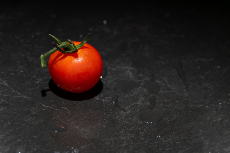 Single Tomato on Black Stone. A single red tomato with water drops lies on a dark stone floor. Reduced to the essentials.の写真素材