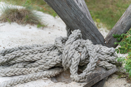 A thick, braided rope lies on sandy ground, wrapped around a wooden post. The scene is reminiscent...