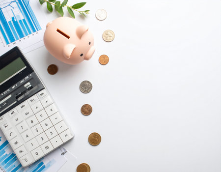 Finances and Saving with Space for Text. A piggy bank, coins, and a calculator lie on a white background. Financial topics are stylishly presented with copy space.の素材