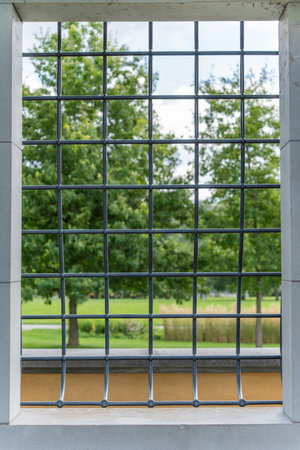 View Through Metal Grid. A square metal grid frames a scenic view of green trees and tall grass in a...