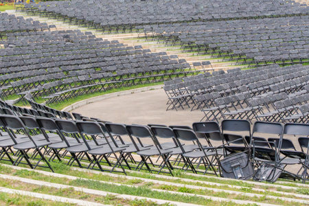 Rows of black folding chairs arranged in curves at an outdoor arena. The quiet venue awaits the...