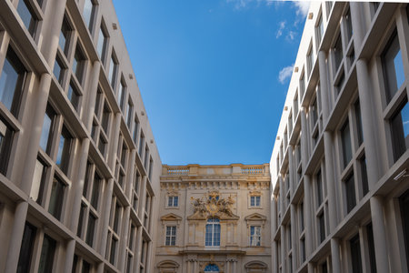 A narrow urban corridor with modern facades frames a historic baroque building. Clear sky highlights the architectural contrast.の写真素材