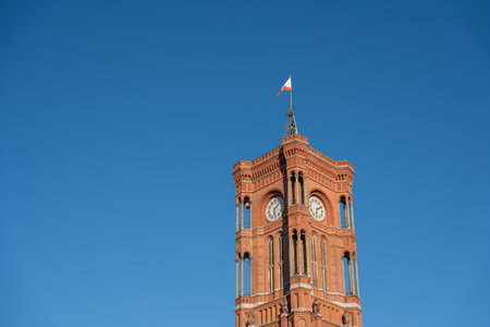 The red-brick Rotes Rathaus tower stands tall under a clear blue sky. The flag waves proudly at the...