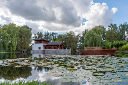 A traditional Chinese building is reflected in the lake. Water lilies and a wooden boat complement the peaceful scene.の写真素材