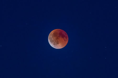 A glowing blood moon dominates the deep blue night. The lunar eclipse creates a mystical atmosphere.の写真素材