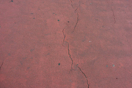 Red Floor with Cracks. Red asphalt or pavement with visible cracks. Texture and wear characterize the surface.の写真素材