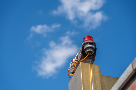Warning Light on Building. Detail of a red warning light on a building roof. Cables and technology are clearly visible against a blue sky.の写真素材