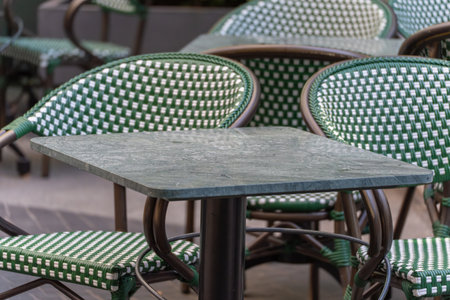 Empty green and white cafe chairs and a marble table await guests. The scene appears calm and inviting.の写真素材