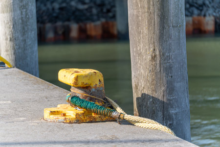A yellow bollard at the harbor secures a ship's rope. The old metal shows traces of rust.