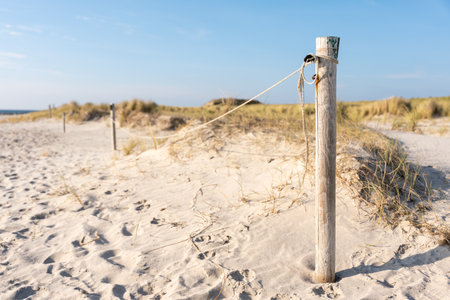 A wooden post with rope marks the dunes. Footprints cover the soft sand beneath the afternoon sun.の写真素材