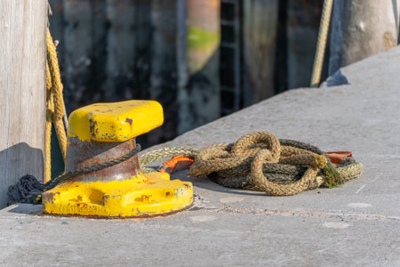 Yellow bollard with ropes harbor detail. A yellow bollard with thick ropes rests on a concrete pier. The scene shows maritime atmosphere.の写真素材